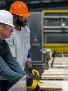 2 men one in white hat and other in orange shown working in a manufacturing unit wearing hard hat