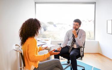 Photograph of a professional office setting showing two people engaged in a conversation, in a counseling session. 