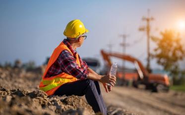 Construction worker taking a water break while overlooking a worksite in the background
